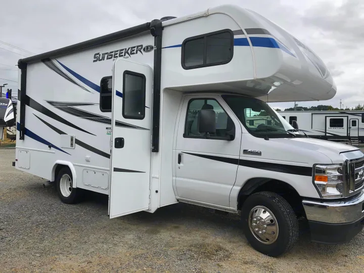 Bright white Sunseeker LE Class C rv rental with an open side door, parked on a gravel lot under a cloudy sky.. Forest River Sunseeker 2021