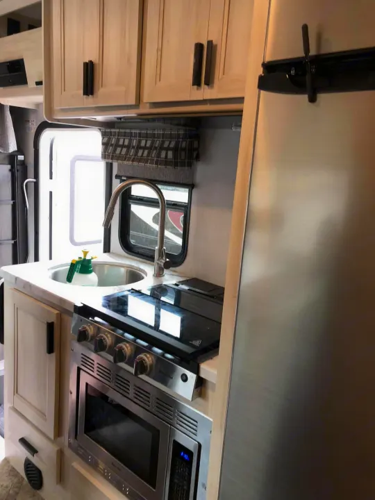 Modern RV rental kitchen with stainless steel fridge, stove, microwave, and sink. Light wood cabinets above.. Forest River Sunseeker 2021