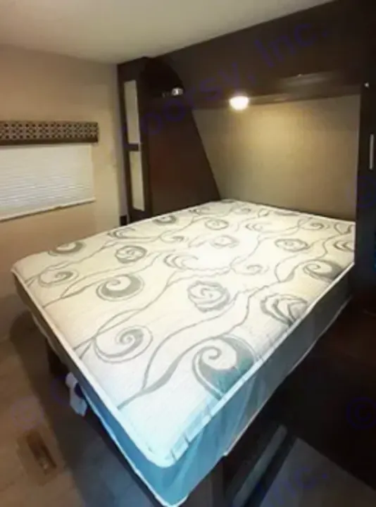 Inside an RV rental, a comfy queen bed with a patterned mattress cover, overhead storage, and reading lights.. KZSP Sportsman 260 2019