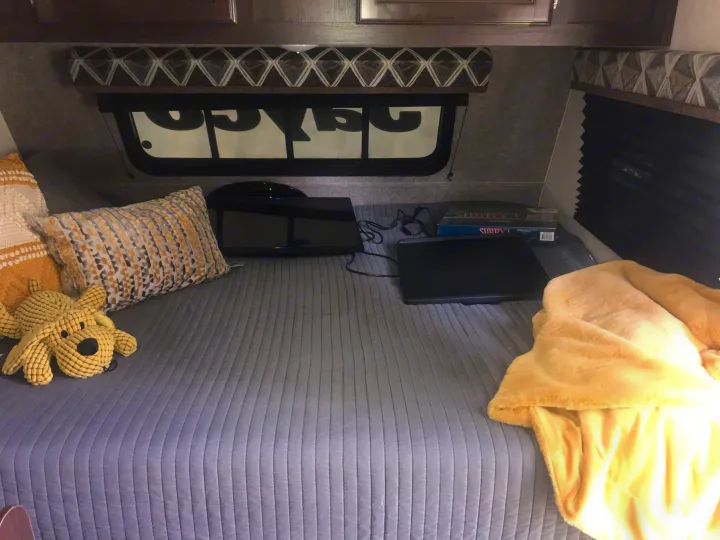 Inside an RV rental: a cozy bed with TV, laptop, game, pillows, and a soft blanket for relaxing travel.. Jayco Jay Flight 2019