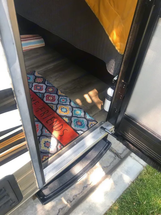 View into an RV rental entrance showing a 'WELCOME FRIENDS' mat, steps, bedding, and fire extinguisher.. Jayco Jay Flight 2019