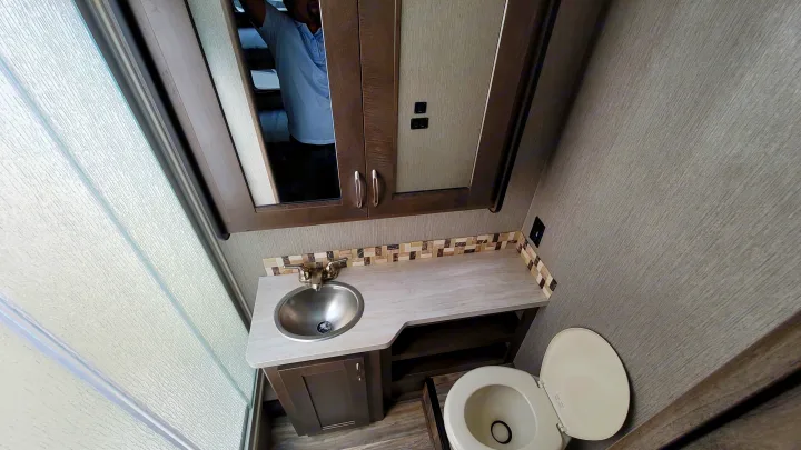 Compact RV rental bathroom featuring a stainless sink, toilet, and textured glass shower door. Ideal for travel.. Nexus Wraith 2022