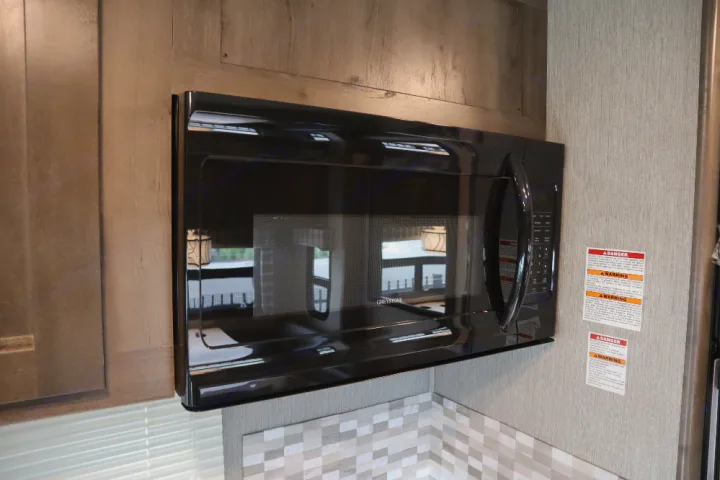 A black Greystone microwave, an essential appliance in this RV rental kitchen, with a patterned backsplash and warning labels visible.. Nexus Wraith 2022