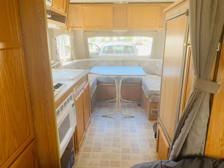Inside an RV rental, featuring a U-shaped dinette, kitchen area with sink and microwave, and ample wood cabinets.. Travel Lite Travel-Lite 800 2003