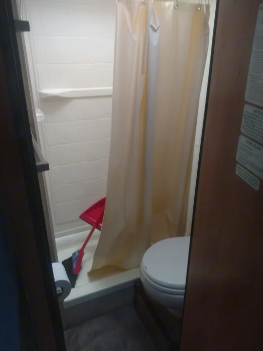 This RV rental bathroom features a compact shower with a red dustpan and brush, toilet, and important notices on the door.. Thor Motor Coach Four Winds Majestic 2013