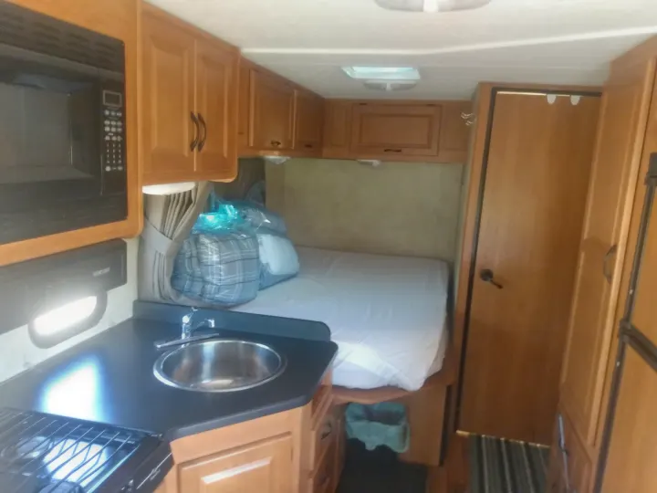 This RV rental interior features a compact kitchen with a microwave, sink, and stovetop, alongside a comfortable bed area.. Thor Motor Coach Four Winds Majestic 2013