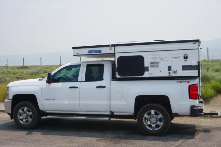 White Chevy 2500HD pickup with Four Wheel Hawk pop-up truck camper. Explore the outdoors with this RV rental!. Chevrolet Silverado 2020