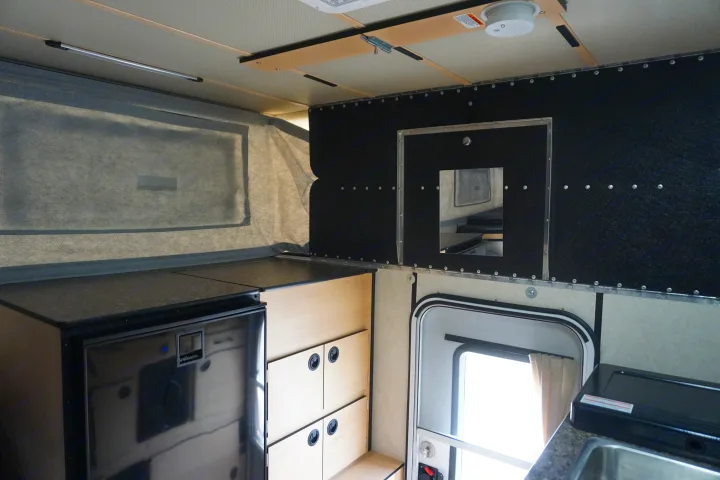 Inside this RV rental: compact kitchen with fridge, wood storage, and view of the pop-top canvas wall. Mobile living.. Chevrolet Silverado 2020