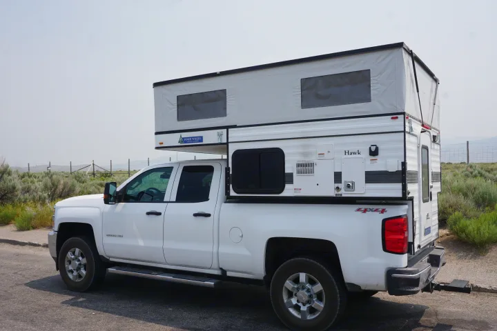 This white pickup truck with a raised Four Wheel Pop-Up Hawk truck camper is ready for an RV rental journey.. Chevrolet Silverado 2020