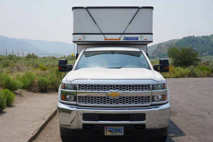 Front view of a white Chevy truck with a pop-up camper, an ideal RV rental for outdoor adventures in Wyoming.. Chevrolet Silverado 2020