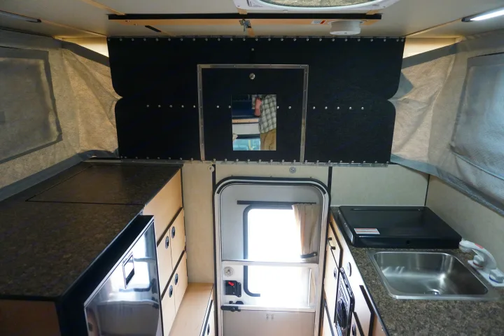 Explore this RV rental's interior: a compact pop-up camper kitchen with sink, stovetop, fridge, and storage.. Chevrolet Silverado 2020