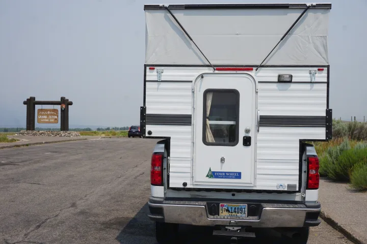 A versatile truck camper, perfect for RV rental adventures, parked at the iconic Grand Teton National Park entrance in Wyoming.. Chevrolet Silverado 2020