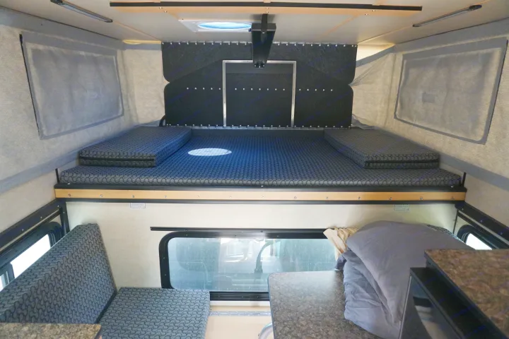 RV rental interior: A bed/lounge area with patterned gray cushions and a dining table on the right.. Chevrolet Silverado 2020