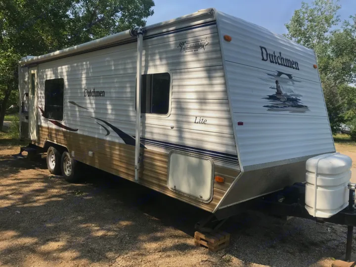 A white and brown Dutchmen travel trailer is parked outdoors, ready for your RV rental adventure.. Dutchmen Dutchmen 2007