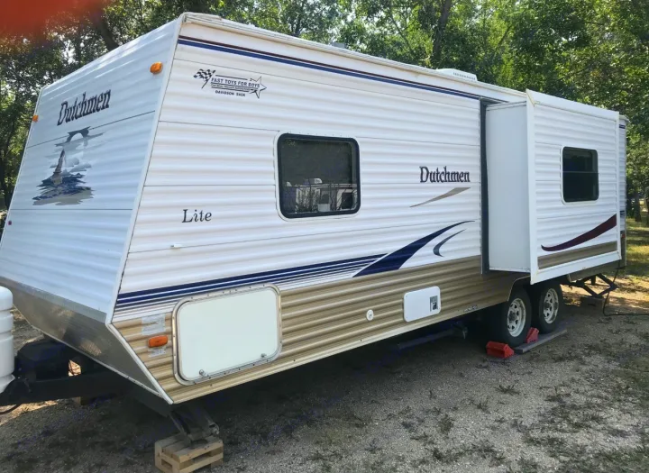 White Dutchmen Lite travel trailer, ideal for an rv rental, parked on gravel with its slide-out extended.. Dutchmen Dutchmen 2007