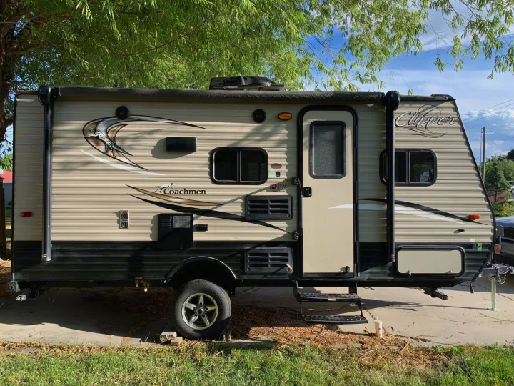 This Coachmen Clipper travel trailer, a tan-colored RV rental, is parked outdoors under green willow branches on a sunny day.. Coachmen Clipper 2017