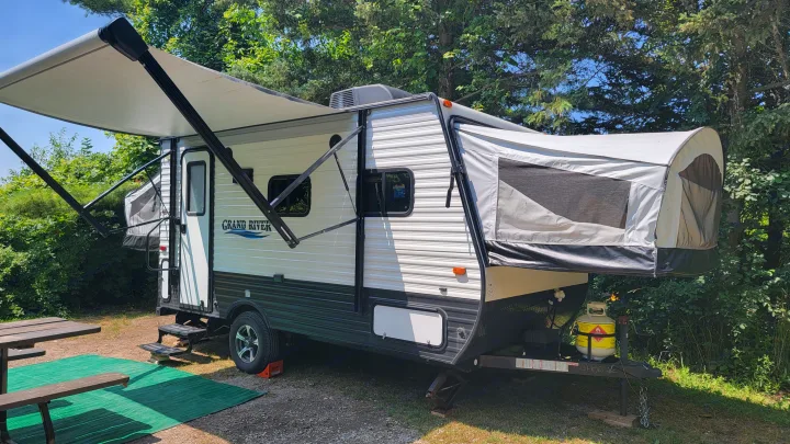 Spacious rv rental camper with extended awning and pop-out sections, parked at a sunny campsite.. Forest River 16RB 2019