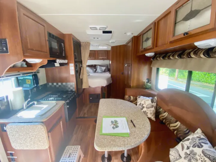 Spacious RV rental interior: kitchen on left, dining booth on right, and bed at rear. Wood accents throughout.. Forest River Coachmen Leprechaun 2014