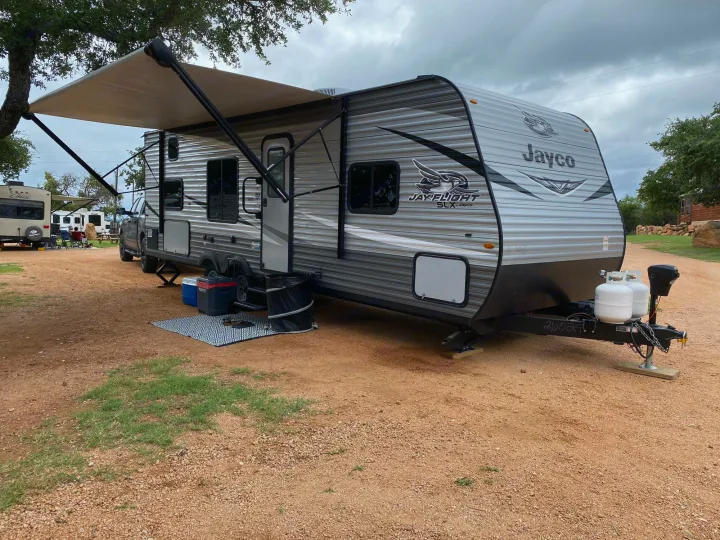 RV rental ready for adventure: A grey Jayco travel trailer with an extended awning at a spacious, rustic campsite.. Jayco Jay Flight SLX 2021