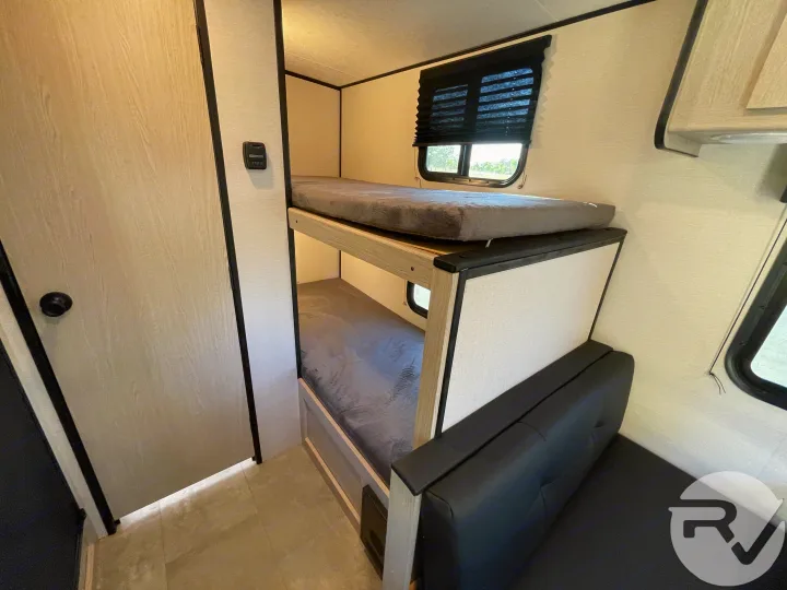 RV rental interior: Bunk beds with grey mattresses, a sofa, and a window. Ideal for family travel.. Coachmen Apex 2021