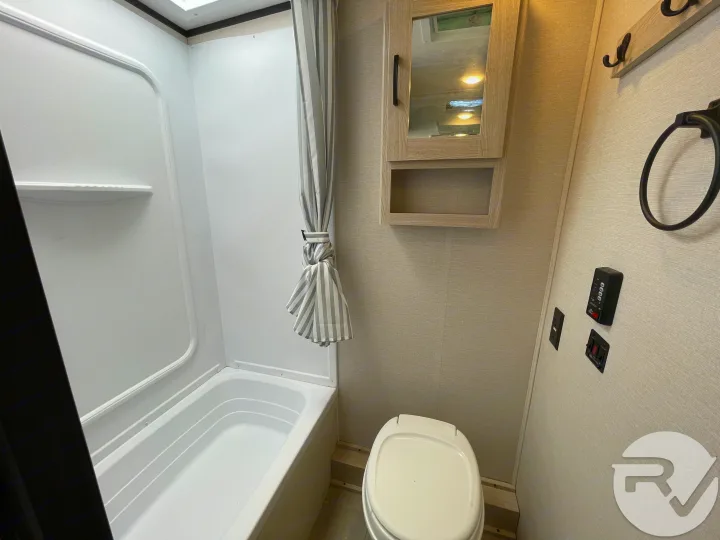 Clean RV rental bathroom with tub, shower, toilet, and mirrored cabinet.. Coachmen Apex 2021