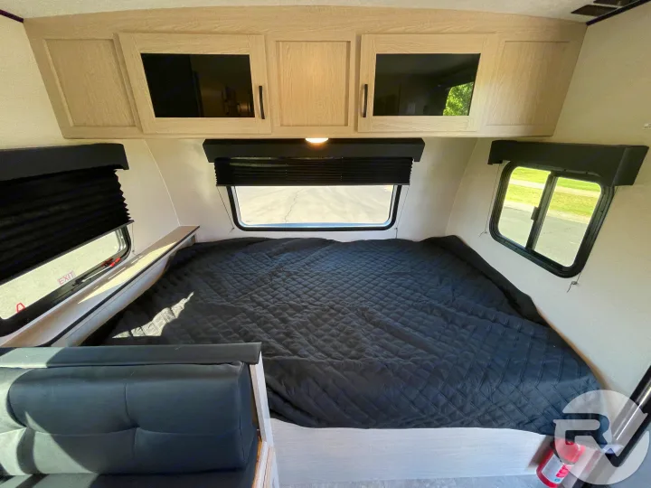 This RV rental bedroom features a comfy black bed, overhead cabinets, and essential safety items like an exit window and extinguisher.. Coachmen Apex 2021