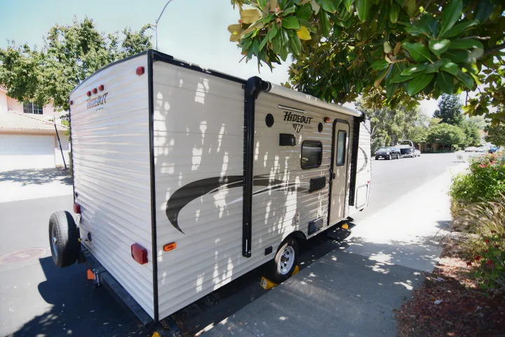 A light-colored Hideout RV rental, safely parked on a sunny residential street with chocks, awaits your next trip.. Keystone RV Hideout 2017