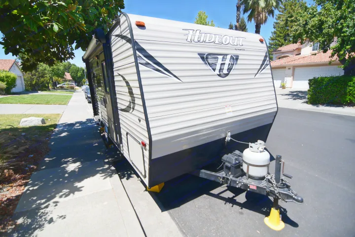 Hideout travel trailer, possibly an RV rental, parked on a sunny residential street with trees overhead.. Keystone RV Hideout 2017