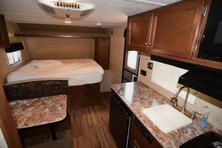 Cozy RV rental interior featuring a comfortable bed, functional kitchen with sink, dining area, and overhead cabinets.. Keystone RV Hideout 2017
