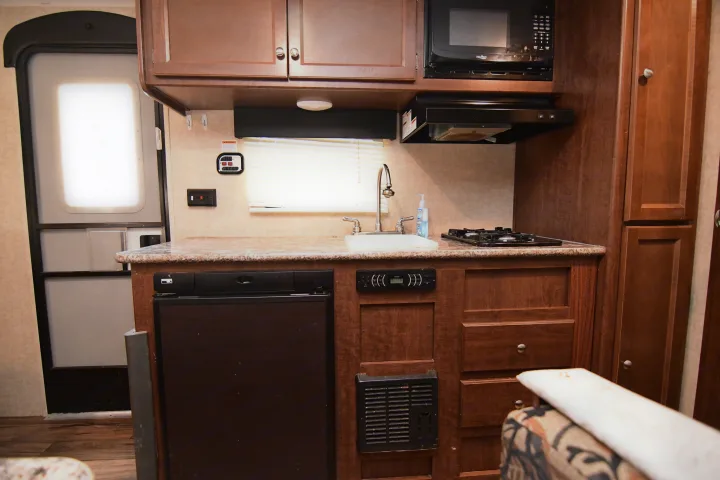 View of an RV rental's cozy kitchen with a sink, two-burner stove, microwave, and refrigerator for on-the-go cooking.. Keystone RV Hideout 2017