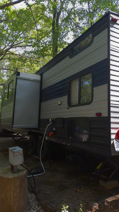 Side view of an RV rental with its slide-out extended, hooked up for camping amidst trees.. Forest River Cherokee Grey Wolf 2021