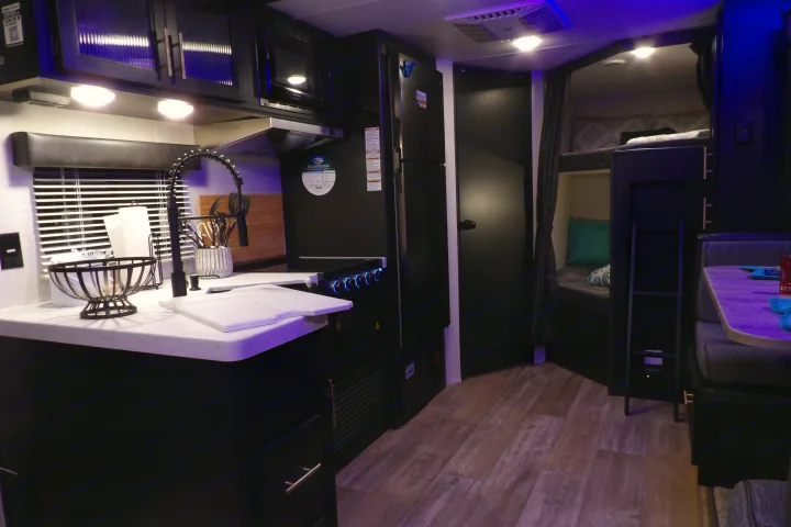 Explore this RV rental's sleek interior: a modern kitchen, refrigerator, bunk beds, and dining area, all bathed in accent lighting.. Forest River Cherokee Grey Wolf 2021