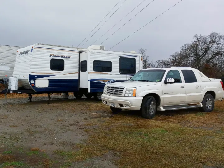 A white "Traveler" RV rental and a Cadillac Escalade EXT are parked on a muddy lot under a grey sky.. Holiday rambler Traveler 2013