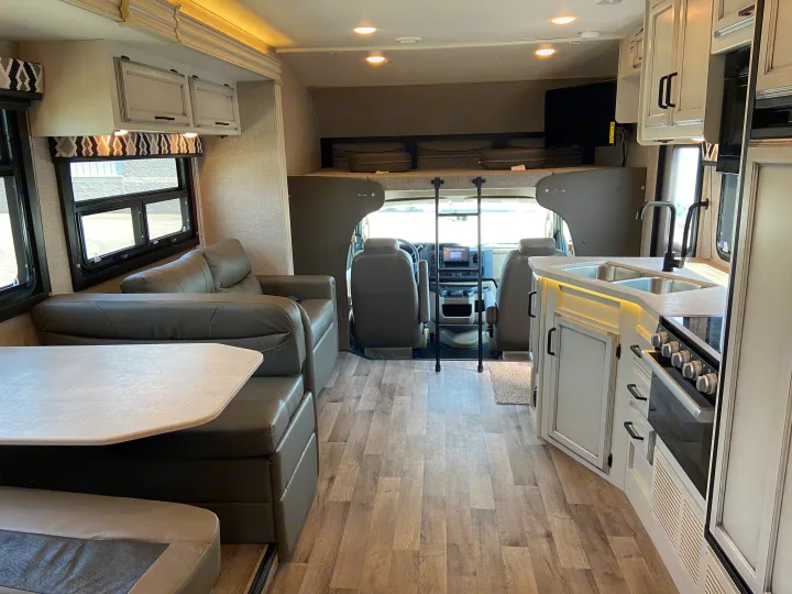 Inside a modern RV rental: view from rear showing kitchen, dining table, sofa, & cab-over bunk sleeping area.. Jayco Redhawk 2025