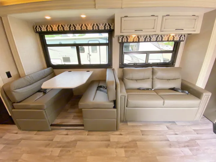 Inside a well-appointed RV rental, showcasing a comfortable dinette booth and a convertible sofa in a bright living area.. Jayco Redhawk 2025