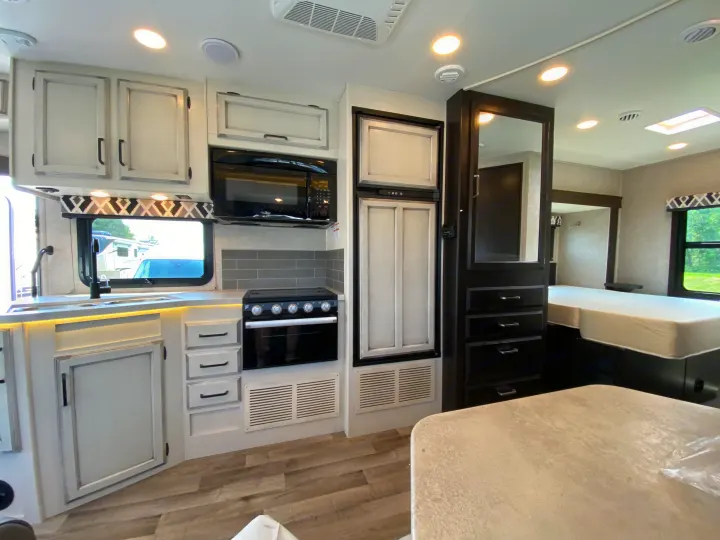 Inside a modern RV rental, featuring a full kitchen with light cabinetry and a cozy bedroom area.. Jayco Redhawk 2025