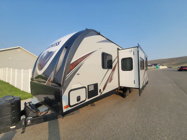 Modern gray and black travel trailer RV rental with pop-out extended, parked on asphalt.. Heartland RVs Wilderness 2020