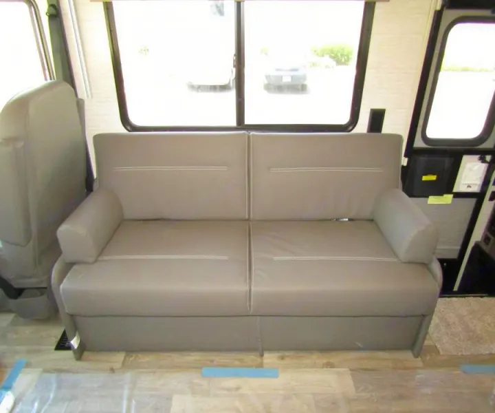 Interior of an RV rental: a modern grey sofa with stitched details, set against large windows, ready for your next adventure.. Winnebago Vista 2022