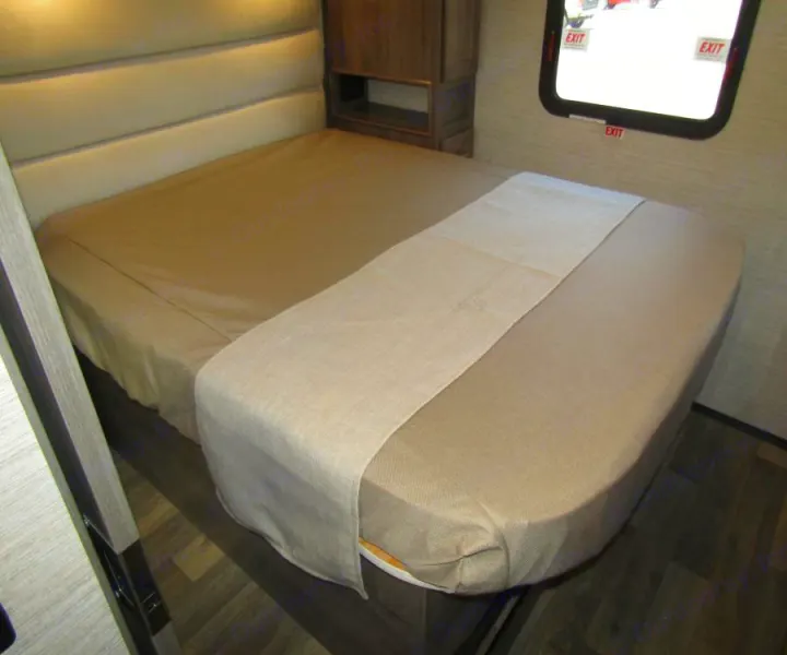 Cozy RV rental bedroom with a neatly made bed featuring light brown bedding and a beige runner. Perfect for compact living.. Winnebago Vista 2022