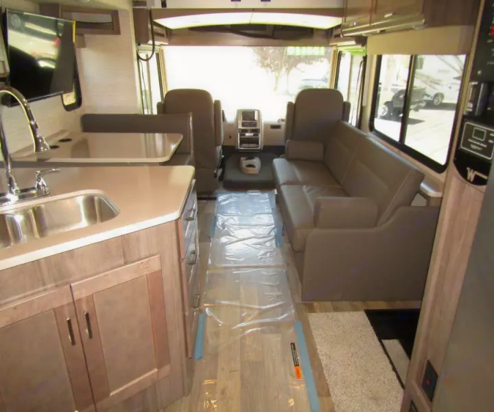 RV rental interior. View of kitchen with sink, dinette, living room sofa, and front cockpit. Protective floor covering.. Winnebago Vista 2022