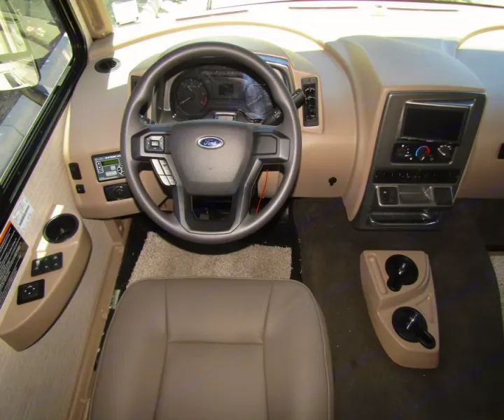 RV rental cockpit: Tan driver's area, Ford steering wheel, dashboard, and controls ready for your journey.. Winnebago Vista 2022