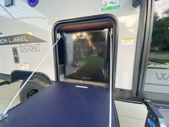 Visually, an open RV compartment reveals a Hotpoint mini-fridge and an extended counter. This RV rental offers a convenient outdoor kitchen setup.. Forest River Other 2021