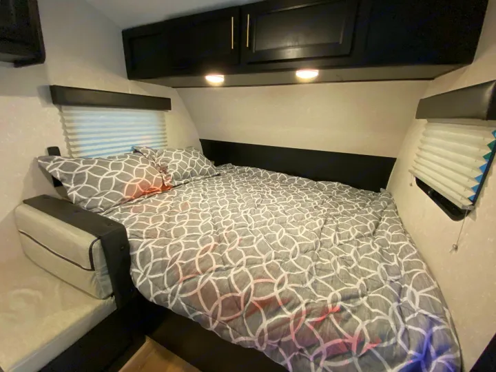 Cozy RV rental bedroom featuring a bed with patterned comforter, overhead cabinets, and windows with blinds.. Forest River Other 2021