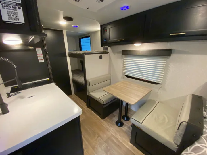 RV rental interior view: modern kitchen area, a comfortable dinette with table, and compact bunk beds. Light wood flooring.. Forest River Other 2021