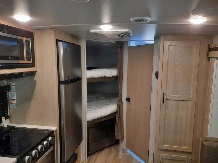 RV rental interior: Modern kitchenette with microwave, stove, fridge, and adjacent bunk beds.. Forest River Rockwood Mini Lite 2021