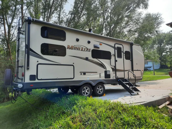 Light-colored Rockwood Mini Lite RV rental parked on a concrete pad, partially on grass, with trees in the background.. Forest River Rockwood Mini Lite 2021