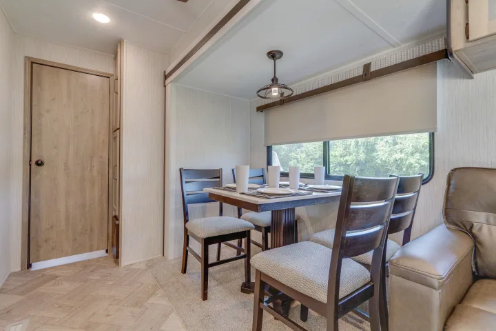 This RV rental interior features a well-lit dining area with a table and four chairs, perfect for meals on the road.. Palomino Puma Park Trailer for Temporary Housing 2021