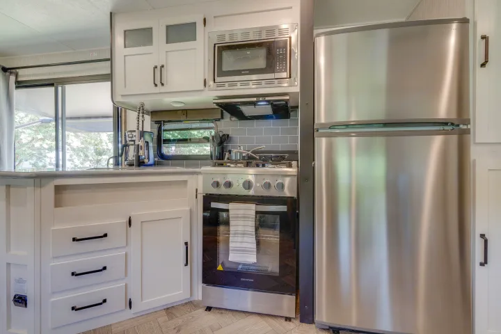 Modern RV rental kitchen featuring stainless steel appliances like a microwave, stove, and refrigerator.. Palomino Puma Park Trailer for Temporary Housing 2021