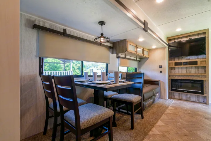 Bright RV rental interior featuring a modern dining area, comfortable seating, TV, and electric fireplace.. Palomino Puma Park Trailer for Temporary Housing 2021