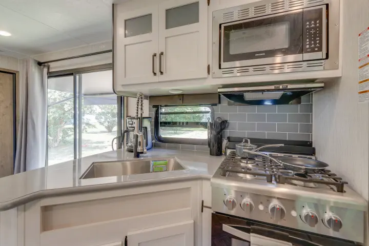 Functional RV rental kitchen featuring a microwave, gas stove, sink, and counter space. Ready for your next travel adventure.. Palomino Puma Park Trailer for Temporary Housing 2021